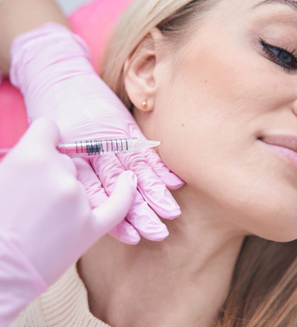 Female getting cheek filler injection under skin of cheekbone by plastic surgeon